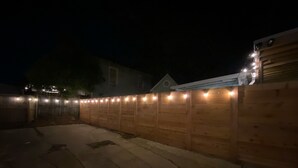 Vista nocturna de un patio trasero con valla de madera y luces colgantes.
