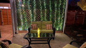 Un área de estar al aire libre con una mesa de vidrio, dos sillas de mimbre y un sofá verde con almohadones a rayas.