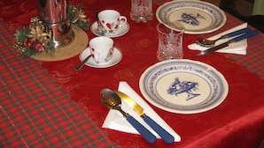 Une table dressée avec une nappe rouge, des assiettes blanches et bleues, un pichet en argent, un verre, une cuillère et un couteau.