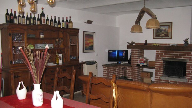 Un salon avec une table rouge, des chaises en bois, une cheminée en briques et un téléviseur.