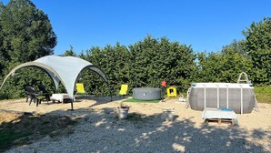 Een camping met een tent, stoelen, een huisje en een opblaasbaar zwembad.