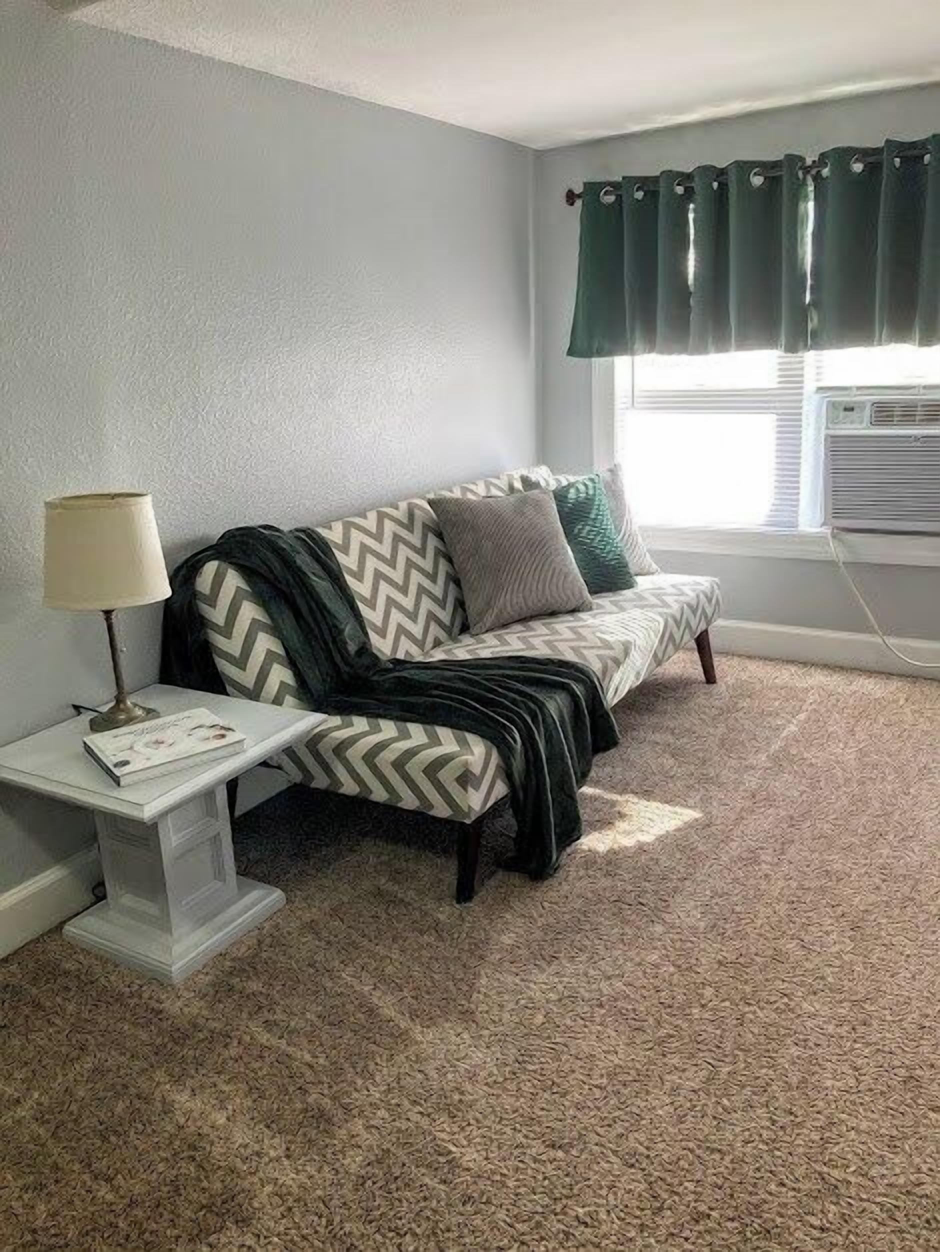 A room with a sofa, a lamp, and a window with curtains.