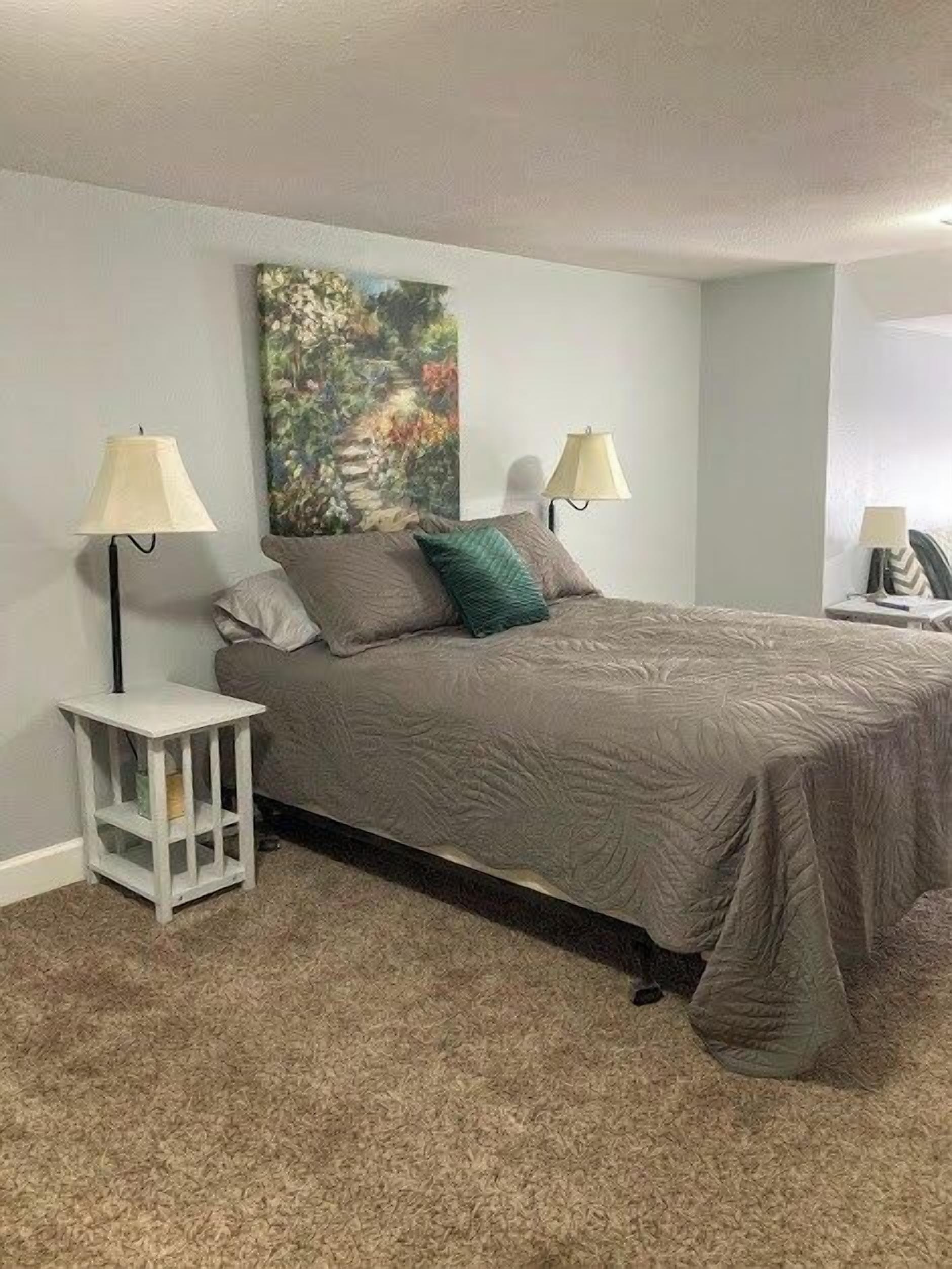 Quarto com cama, duas luminárias de cabeceira, mesa de cabeceira e um quadro na parede.