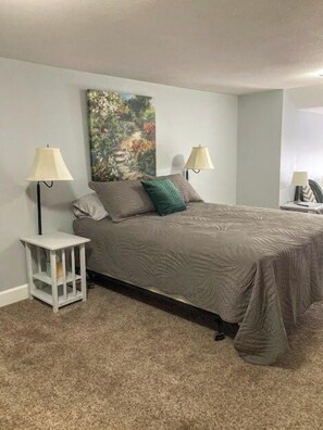 A bedroom with a bed, two bedside lamps, a nightstand, and a painting on the wall. - Stay Awhile Your Comfortable Stay (Hutchinson)