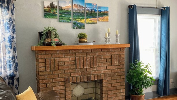 A living room with a brick fireplace, a leather sofa, and a large window with blue curtains.