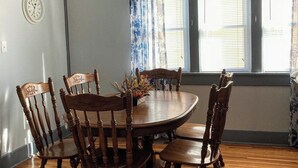 A dining room with a wooden table and chairs, a chandelier, a clock, and a window with blinds.