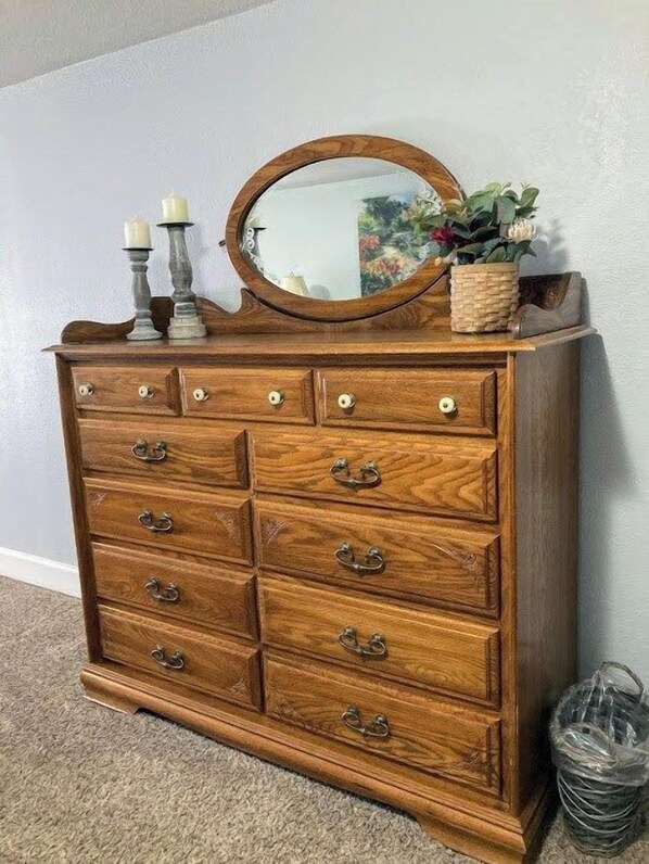 Un aparador de madera con varios cajones y un espejo, junto a velas y una planta en maceta.