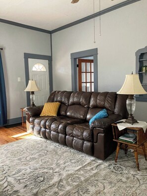 A living room with a brown leather sofa, two lamps, a patterned rug, and a door with a window. - Stay Awhile Your Comfortable Stay (Hutchinson)