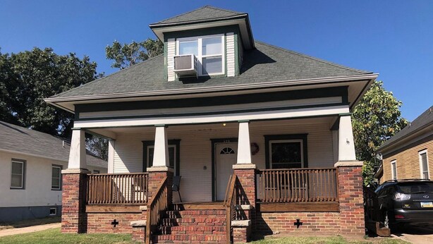 A two-story house with a front porch, a brick base, and a central door.