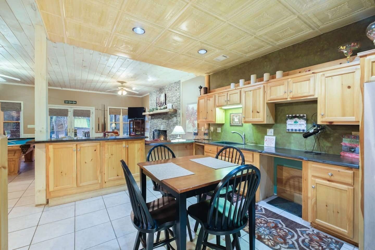 A kitchen with wooden cabinets, a dining table with chairs, a ceiling fan, and a green backsplash.