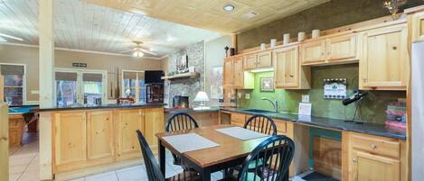 A kitchen with wooden cabinets, a dining table with chairs, a ceiling fan, and a green backsplash.