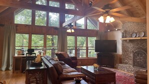 A spacious living room with a large wooden ceiling, a stone fireplace, and a television. - Lake Front, Beautiful views, Gentle slope to Lake, Hot tub, Close to Downtown. (Morganton)