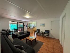 A living room with a sofa, chairs, a coffee table, and a kitchen area in the background. - Fantastic enclosed outdoor area, fully fenced, close to shops, Eurong Beach (Eurong)