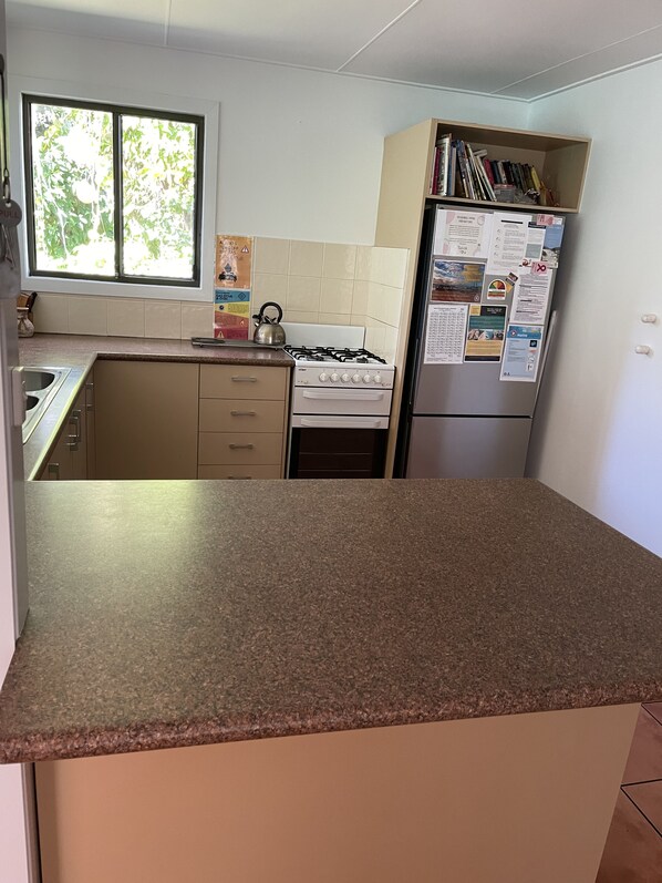 Eine Küche mit Gasherd, Kühlschrank und einem Fenster mit Jalousien.