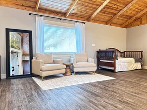 A room with a wooden ceiling, a window with blinds, two armchairs, a small table, a bed with a wooden headboard, and a white rug. - Relaxing 4-BR, Great View, near Beaver Lake and Leatherwood Trails (Eureka Springs)