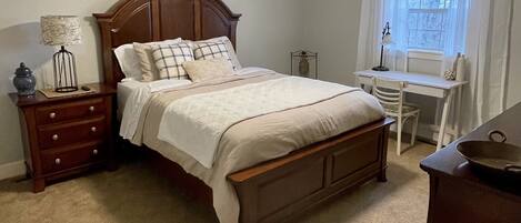 Un dormitorio con cama de madera, mesita de noche, escritorio, silla, ventilador de techo y ventana con cortinas.
