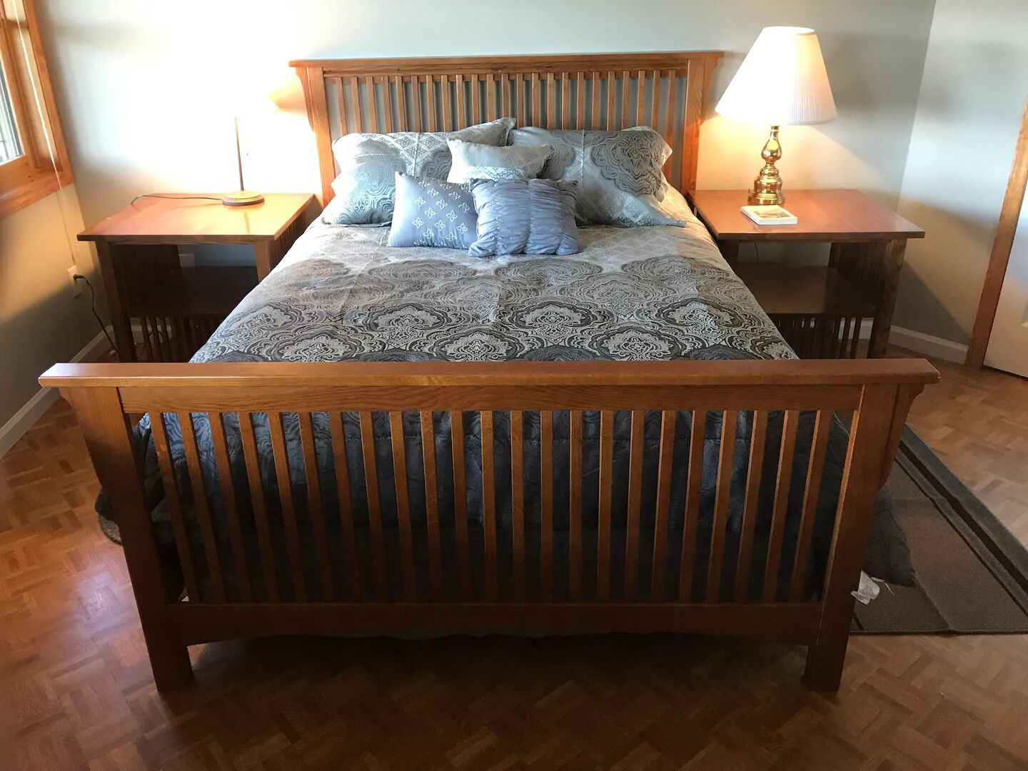 Ein hölzernes Bett mit einem gemusterten Bettbezug und mehreren Kissen, das von Nachttischen mit Lampen gesäumt wird.