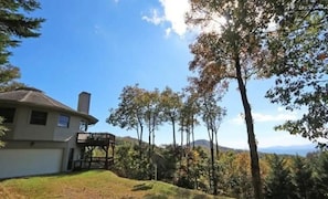 A house with a deck, surrounded by trees and a hilly landscape. - The Big Round Cabin - Blowing Rock, Hot tub, Secluded acreage, fabulous views (Lenoir)