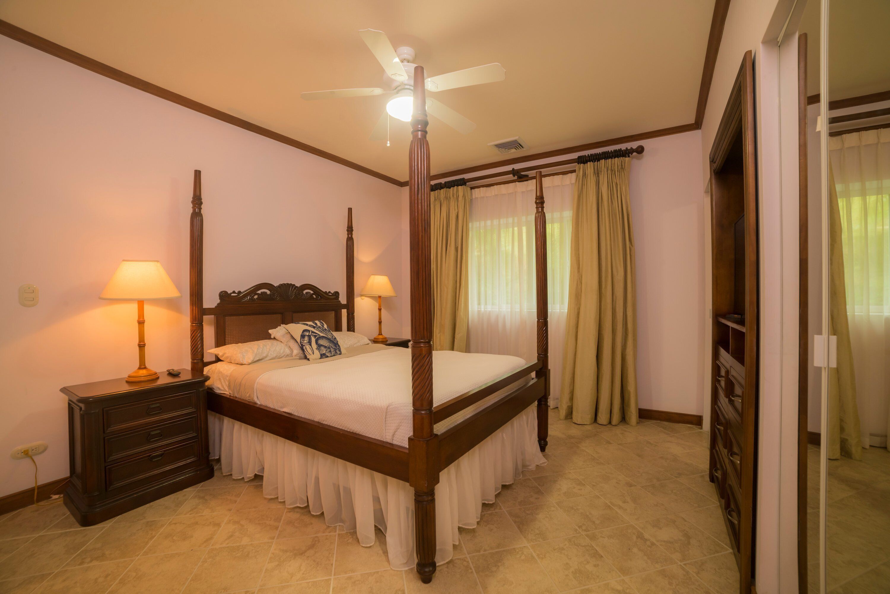 Ein Himmelsbett mit Holzvorhang, zwei Nachttische mit Lampen und ein Deckenventilator.
