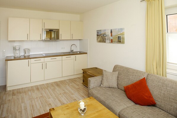A compact living space with a kitchenette, a sofa with a red pillow, and a wooden coffee table.