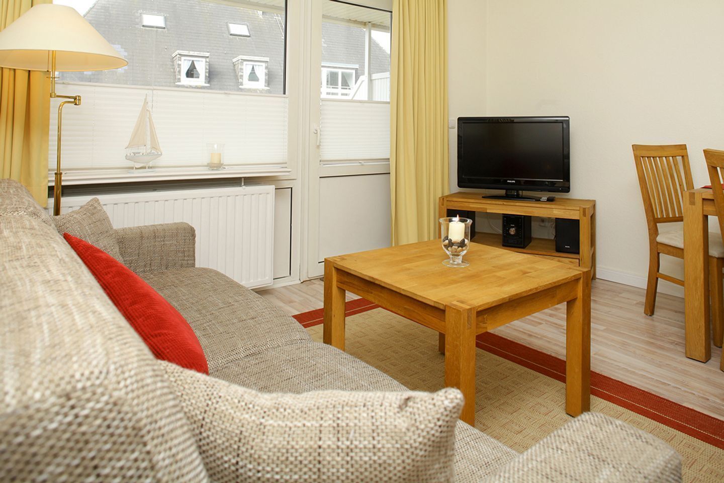 A furnished living room with a sofa, a wooden coffee table, a television on a stand, and a window with curtains.
