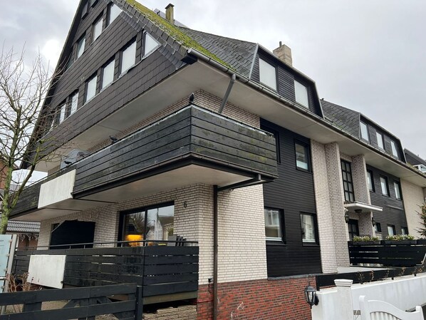 A modern two-story house with a flat roof, large windows, and a balcony.