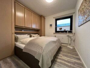 A compact bedroom with a bed, built-in wooden cabinets, a window with a view, and a radiator.