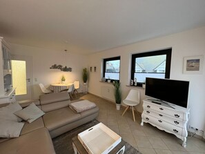 Ein modernes Wohnzimmer mit einer Couch, einem Esstisch, einem Fernseher und einer weißen Kommode.