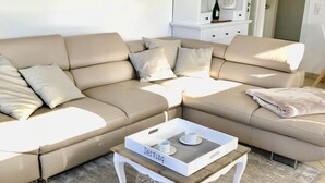 A modern living room with a sectional sofa, a coffee table with a tray labeled 'Serving,' and a cabinet with glass doors. - Margeritenhaus - Relaxed island life: Cozy vacation apartment in Westerland (Sylt)