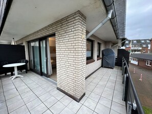 A balcony with a tiled floor, a covered table, and a covered object.