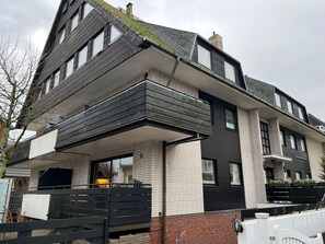 A modern two-story house with a flat roof, large windows, and a balcony.