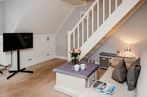 Un salon moderne avec un téléviseur, une table basse avec des tasses, un vase de fleurs, un canapé avec des coussins et un escalier.