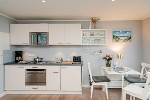 Une cuisine moderne avec des meubles blancs, un four encastré et un coin repas comprenant une table et des chaises.