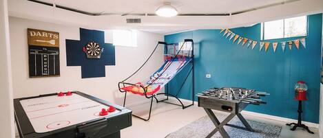 Una habitación con mesa de futbolín, dardos y un mini trampolín.