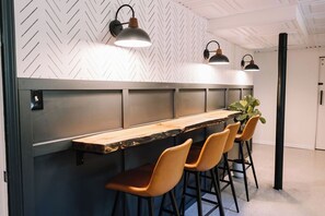 Un espace bar moderne avec un comptoir en bois, quatre tabourets de bar et des luminaires suspendus.