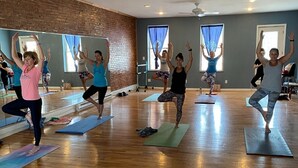 A yoga class in a room with wooden floors and brick walls, large windows with blue curtains, and ceiling fans. - Historic Downtown Hawley Loft (Hawley)