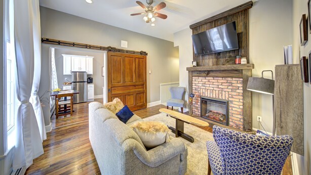 A spacious living room with a fireplace, a ceiling fan, and a kitchen area in the background. - Historic Downtown Hawley Loft (Hawley)