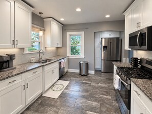 A modern kitchen with white cabinets, stainless steel appliances, and a herringbone-patterned tile floor.