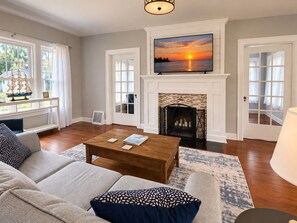 A living room with a fireplace, a television mounted above it, and a large window with a view of the sunset.
