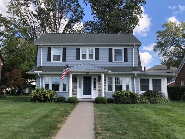 A two-story house with a front porch, an American flag, and a number '1959' on the front door.