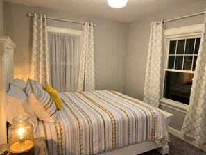 Une chambre à coucher avec un lit, des rideaux, une fenêtre et une table de chevet avec une lampe.