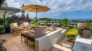 Un patio con mobiliario de mimbre, un paraguas grande y vistas a casas y al océano.