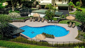 Piscina con sillas de descanso y sombrillas, rodeada de un muro de piedra y vegetación.
