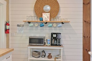 A kitchenette with a microwave, coffee maker, toaster, and a shelf with mugs.