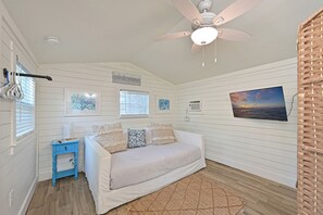 A bedroom with a bed, a ceiling fan, a window with blinds, a wall-mounted air conditioner, and a painting.