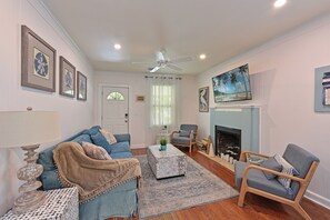 A living room with a sofa, armchair, fireplace, and a ceiling fan. - Historic 1930s Cottage + Heated Pool + 12mi to beaches & 1 mi to downtown (Palmetto)