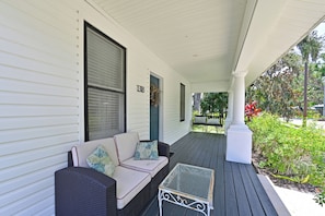 A porch with a white exterior, a number '1318' on the wall, a wicker sofa with cushions, and a small metal table. - Historic 1930s Cottage + Heated Pool + 12mi to beaches & 1 mi to downtown (Palmetto)