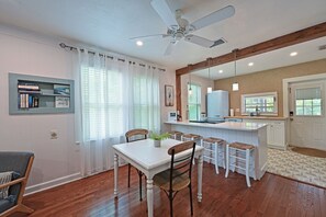 A dining area with a white table, four chairs, a ceiling fan, and a kitchen in the background. - Historic 1930s Cottage + Heated Pool + 12mi to beaches & 1 mi to downtown (Palmetto)