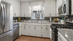 Une cuisine moderne avec des meubles blancs, des appareils en acier inoxydable, un plan de travail en granit et une fenêtre avec un rideau.