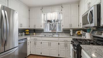 A modern kitchen with white cabinets, stainless steel appliances, a granite countertop, and a window with a curtain.